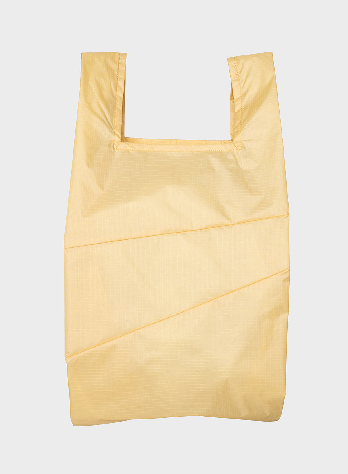A light yellow reusable plastic bag with a wide top opening and shoulder straps, shown flat against a light gray background.