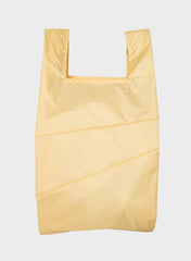 A light yellow reusable plastic bag with a wide top opening and shoulder straps, shown flat against a light gray background.