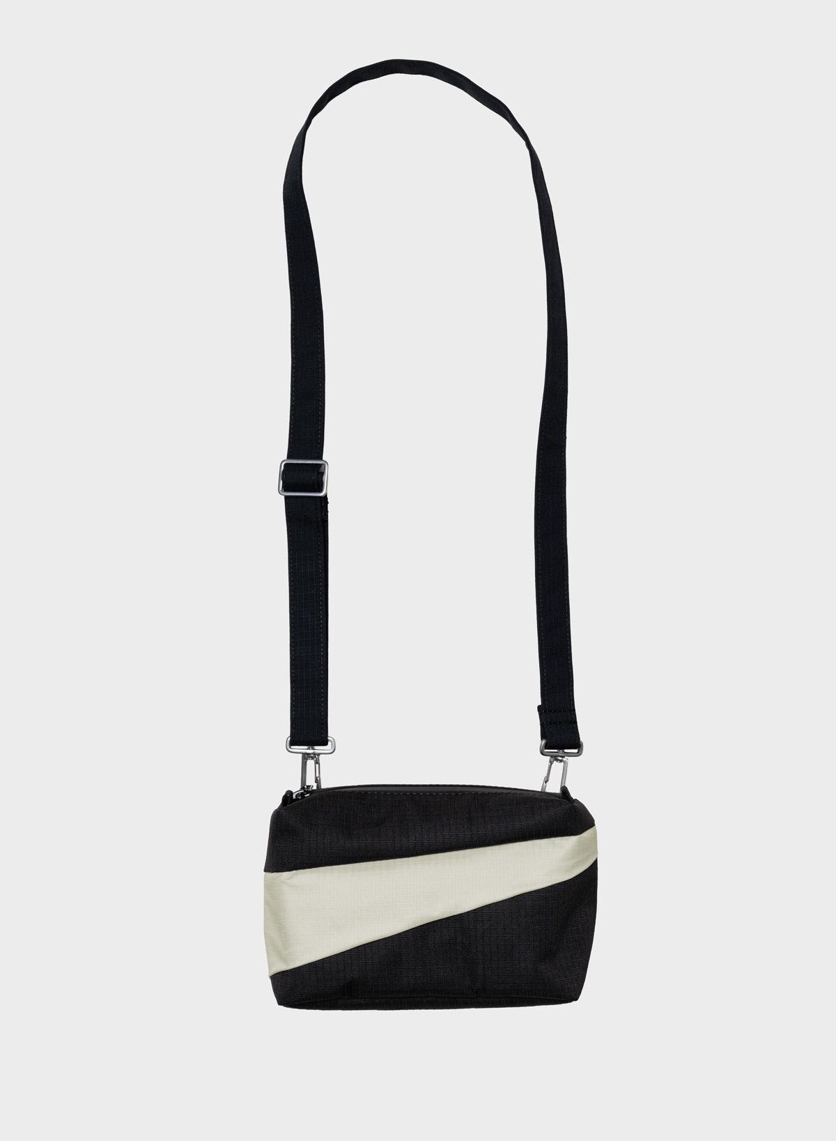 A black and off-white diagonal-striped crossbody bag with a long black shoulder strap, shown against a light gray background.