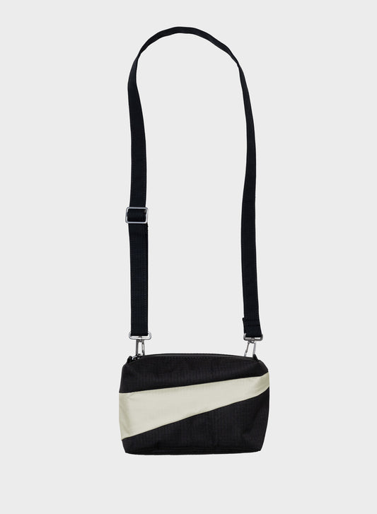 A black and off-white diagonal-striped crossbody bag with a long black shoulder strap, shown against a light gray background.