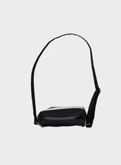 A black crossbody bag with a wide, adjustable black strap and a contrasting light gray horizontal stripe across the front, shown against a plain light gray background.
