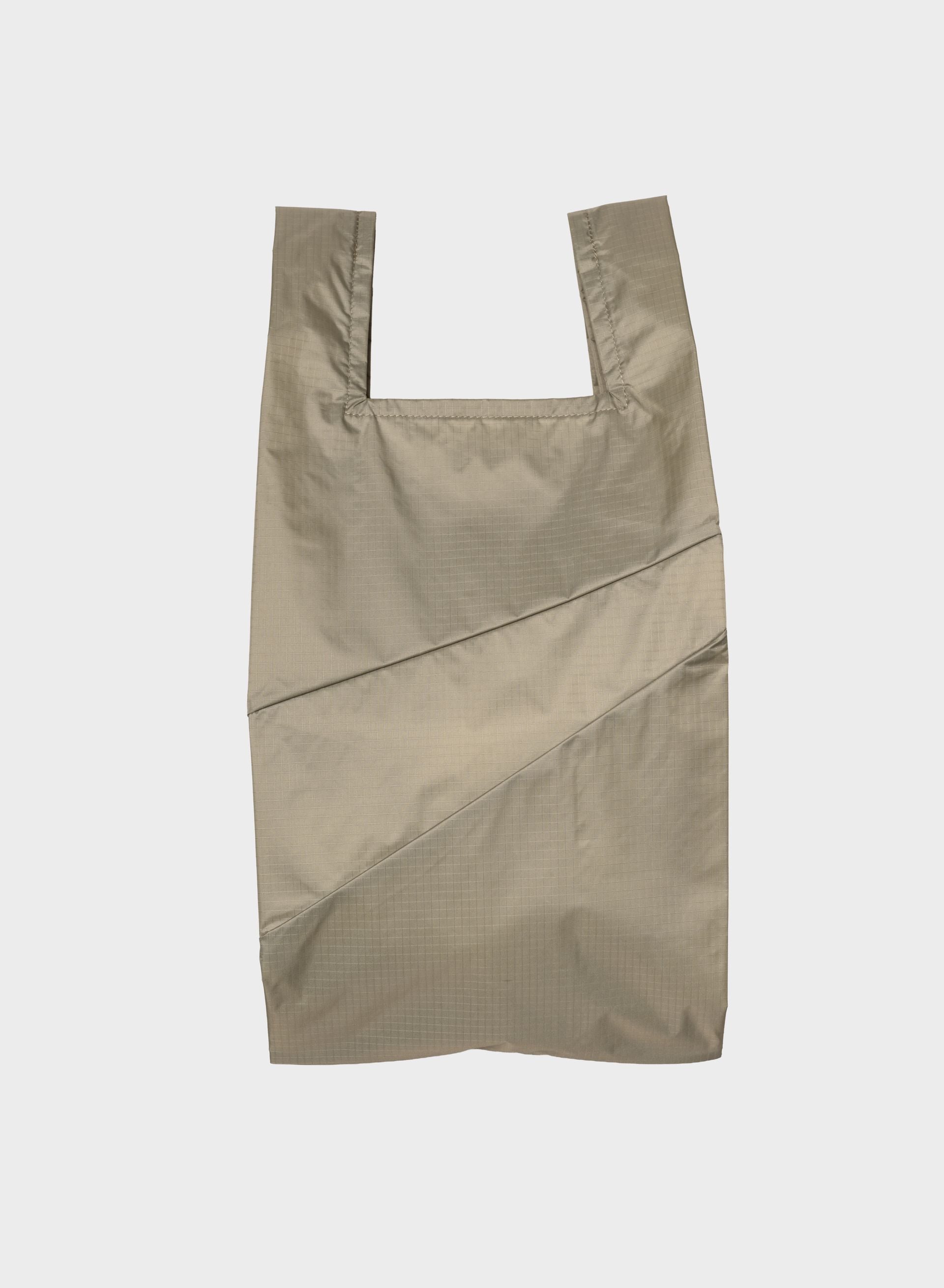 A light beige reusable plastic bag with integrated shoulder straps and diagonal seam details, shown flat against a light gray background.