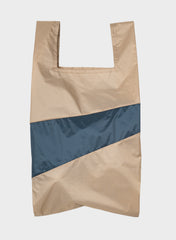 A reusable plastic shopping bag with a color-blocked design, featuring a beige textured upper and lower section divided by a diagonal navy blue panel, shown against a light gray background.