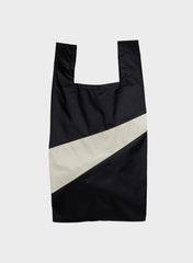 A black reusable plastic bag with a wide diagonal white stripe across the front, photographed flat against a light gray background.