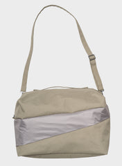 A light beige nylon shoulder bag with a diagonal metallic silver panel on the front and a matching beige adjustable shoulder strap, shown against a light gray background.